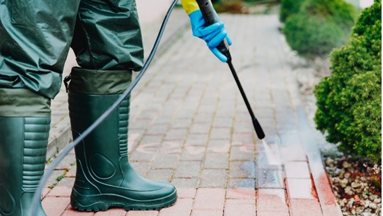 persoon draagt waterdichte kleding en regenlaarzen tijdens het gebruik van hogedrukreiniger